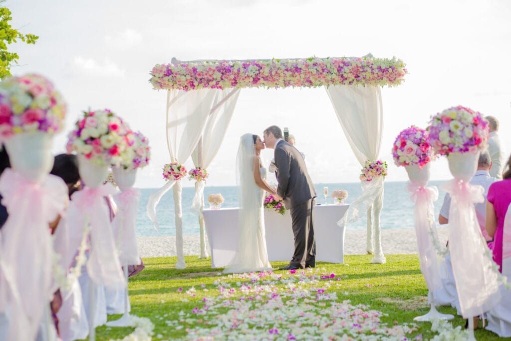 Outdoor wedding ceremony setup, bride and groom under floral arch in sunny weather